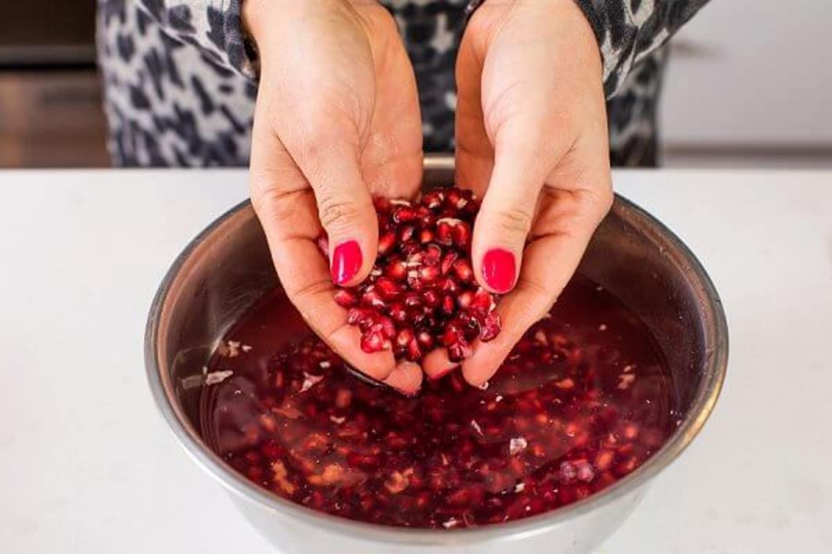 Sorting pomegranate seeds and removing the white pith in a bowl of water.
