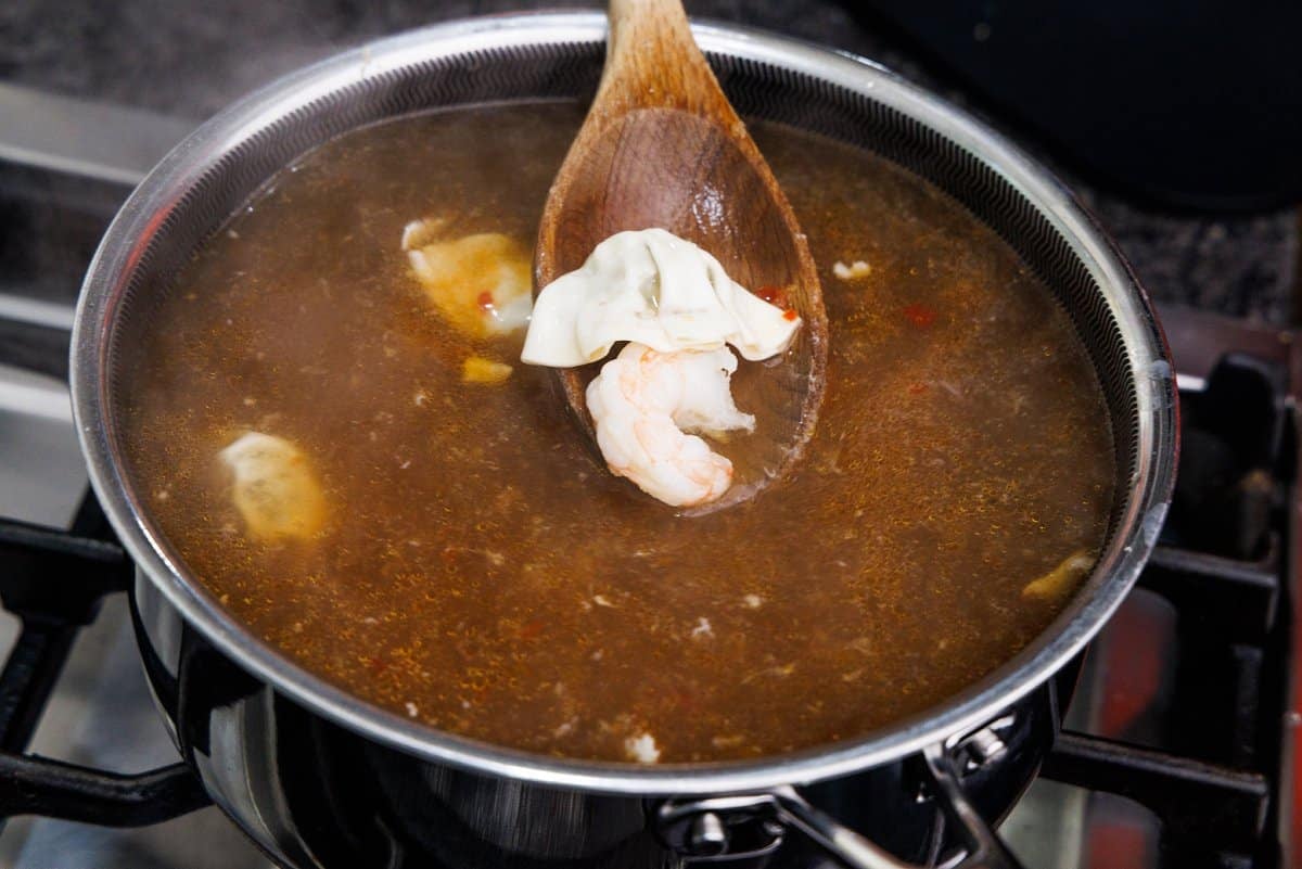 Adding frozen shrimp and dumplings to Asian noodle soup.