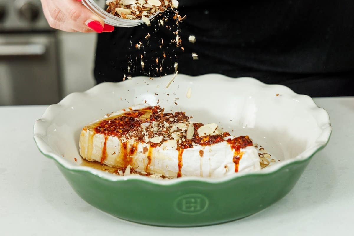 Topping hot honey brie with slivered almonds in a baking dish.