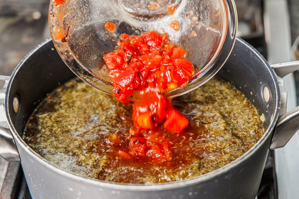 Pouring fire roasted diced tomatoes to a soup pot.