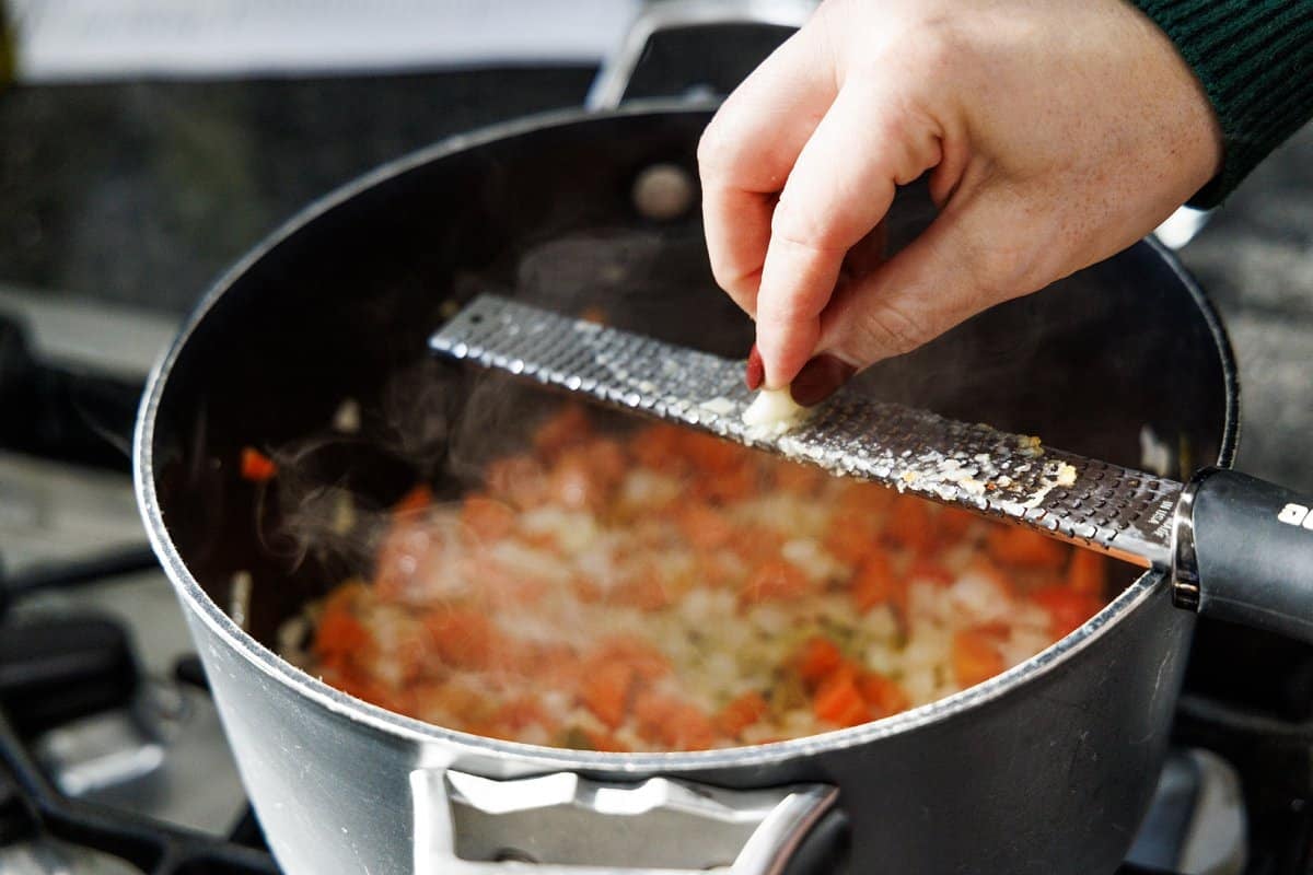 Using a microplane to grate fresh garlic cloves into pot.
