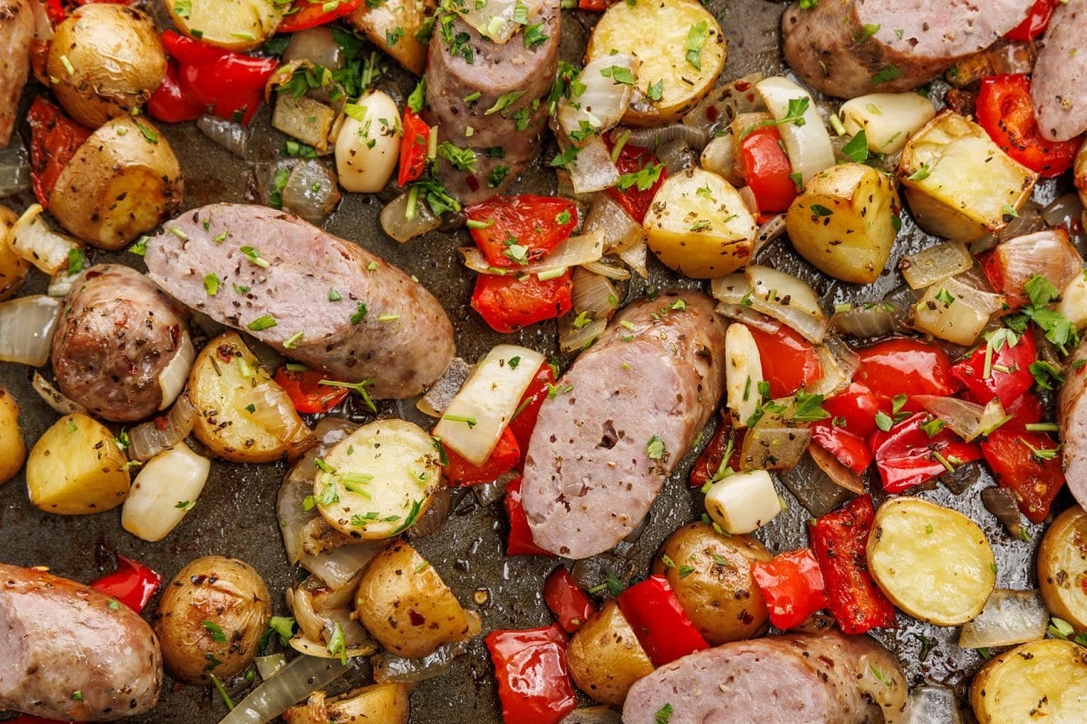 Cooked sheet pan sausage, peppers, and potatoes garnished with fresh parsley.