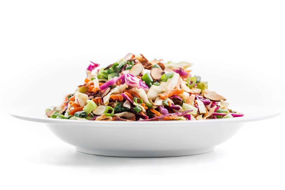 The side view of an entire white deep plate piled with spicy Asian coleslaw.