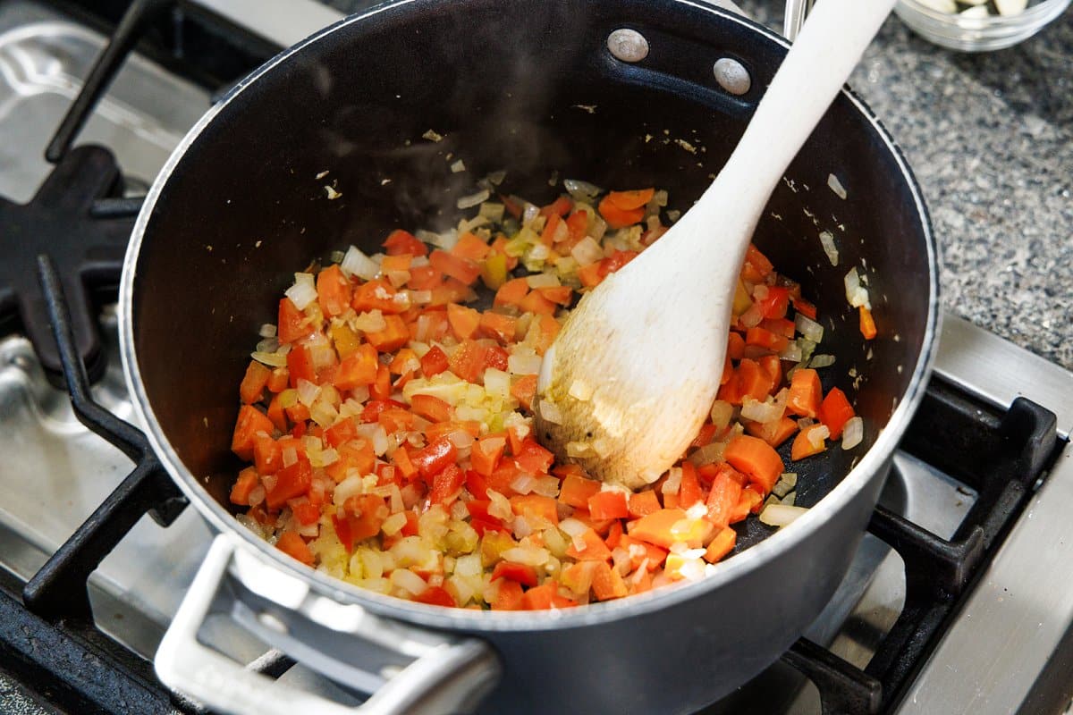 Stirring sautéed veggies in the bottom of a large pot.