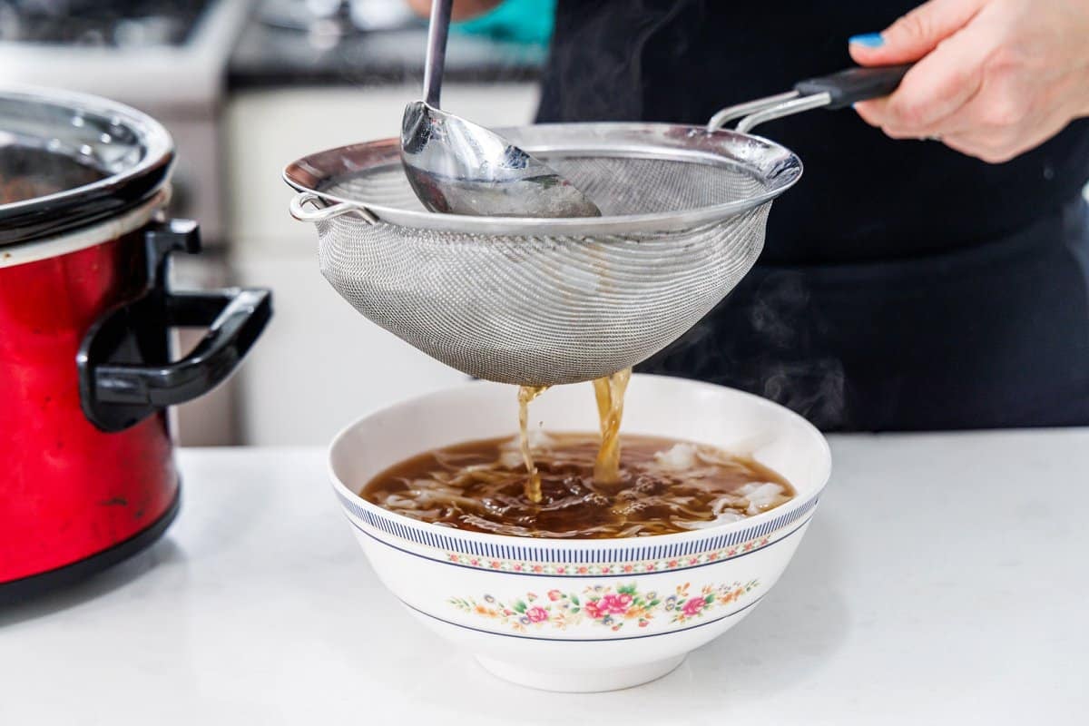 Straining pho broth into bowl.