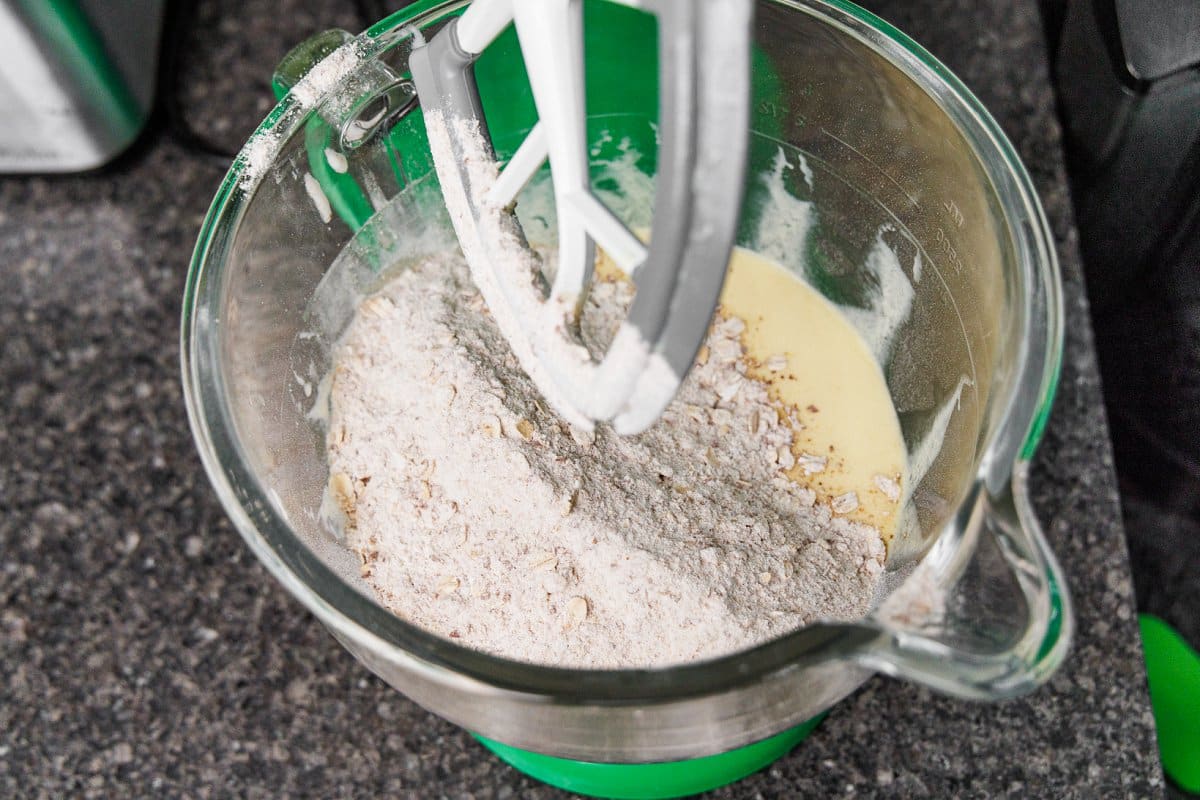 Adding dry ingredients to wet ingredients in the bowl of a stand mixer.