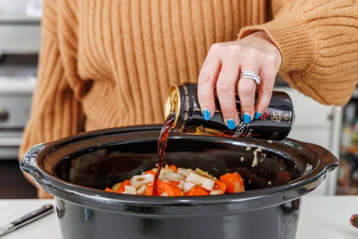 Liz pouring Irish stout into slow cooker with beef and veggies.