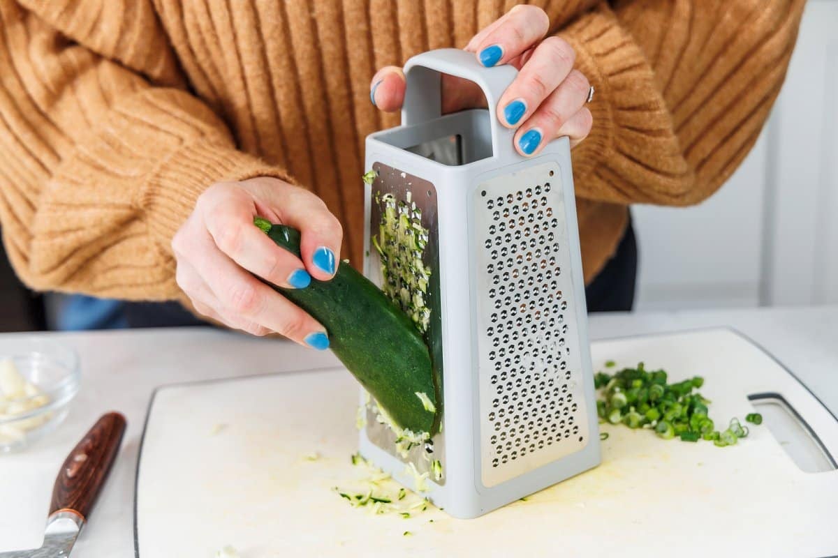 Grating zucchini with a cheese grater onto a cutting board.