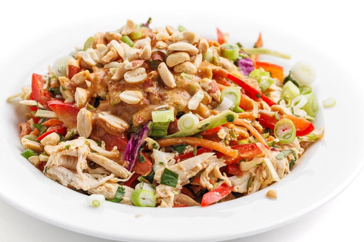 Asian chopped salad in a white bowl topped with dressing and peanuts.