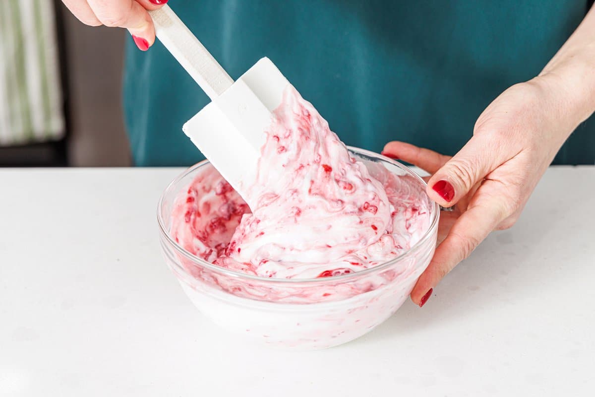 Mixing mashed raspberries and yogurt in a bowl.