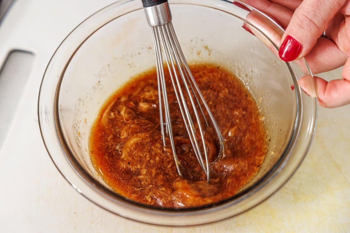 Whisking salad dressing together in a large glass bowl.
