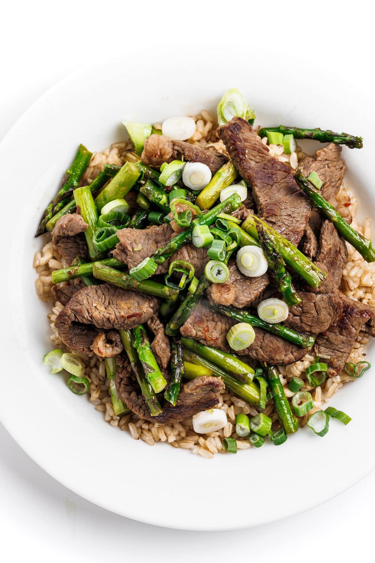 Looking down on a plate of ginger beef and asparagus stir-fry over rice.