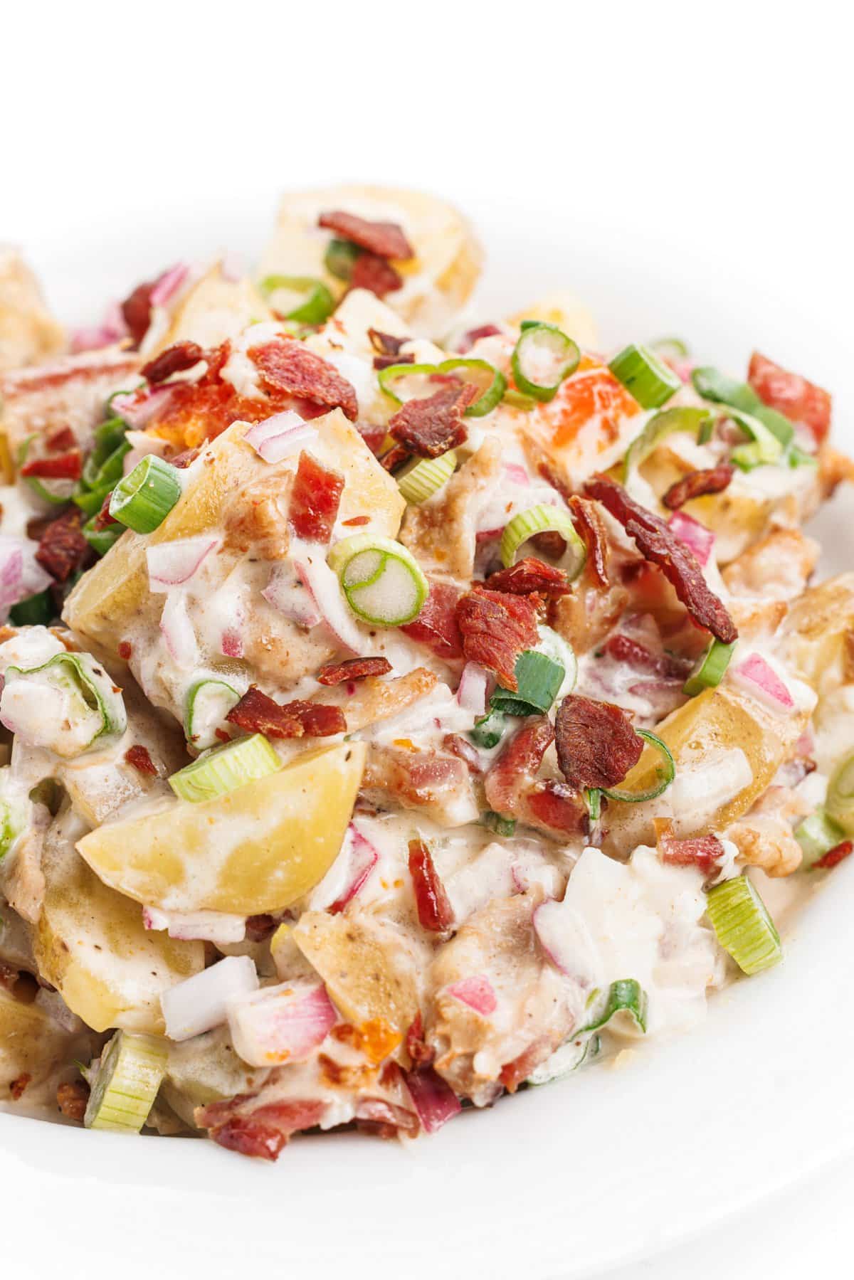 Potato salad with bacon and eggs topped with chives and bacon crumbles.