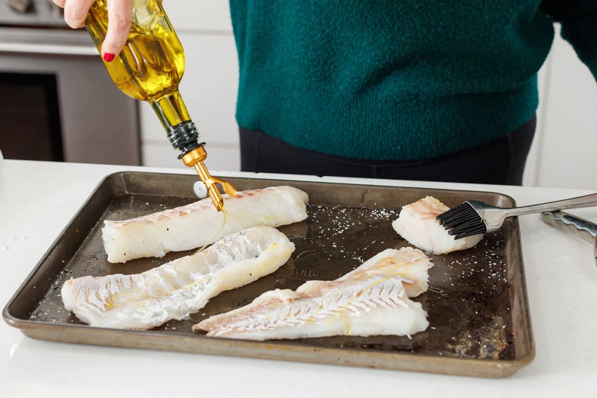Drizzling white fish with olive oil on sheet pan.