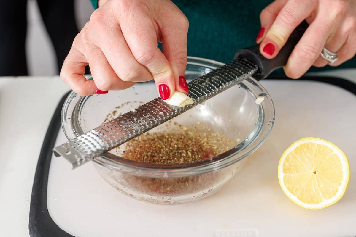 Using a microplane to grate a garlic clove into a glass bowl.
