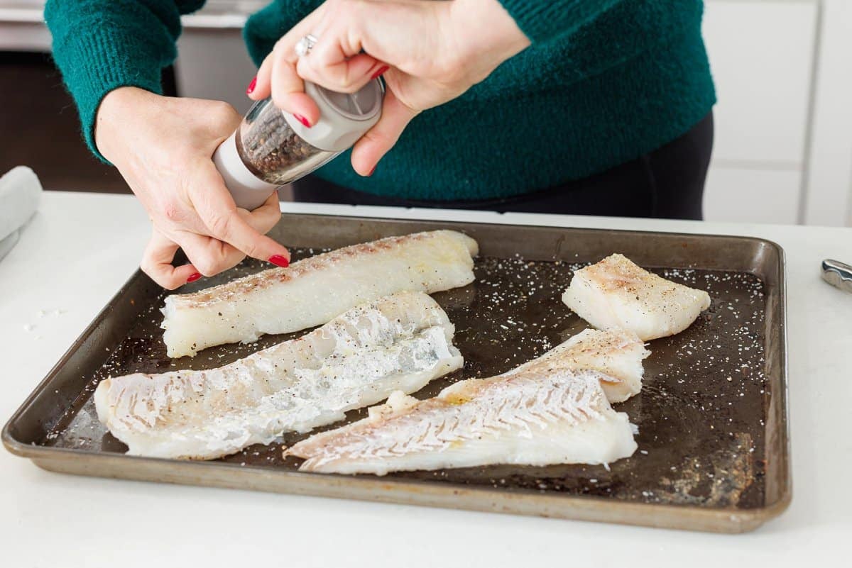 Seasoning whitefish on baking sheet.