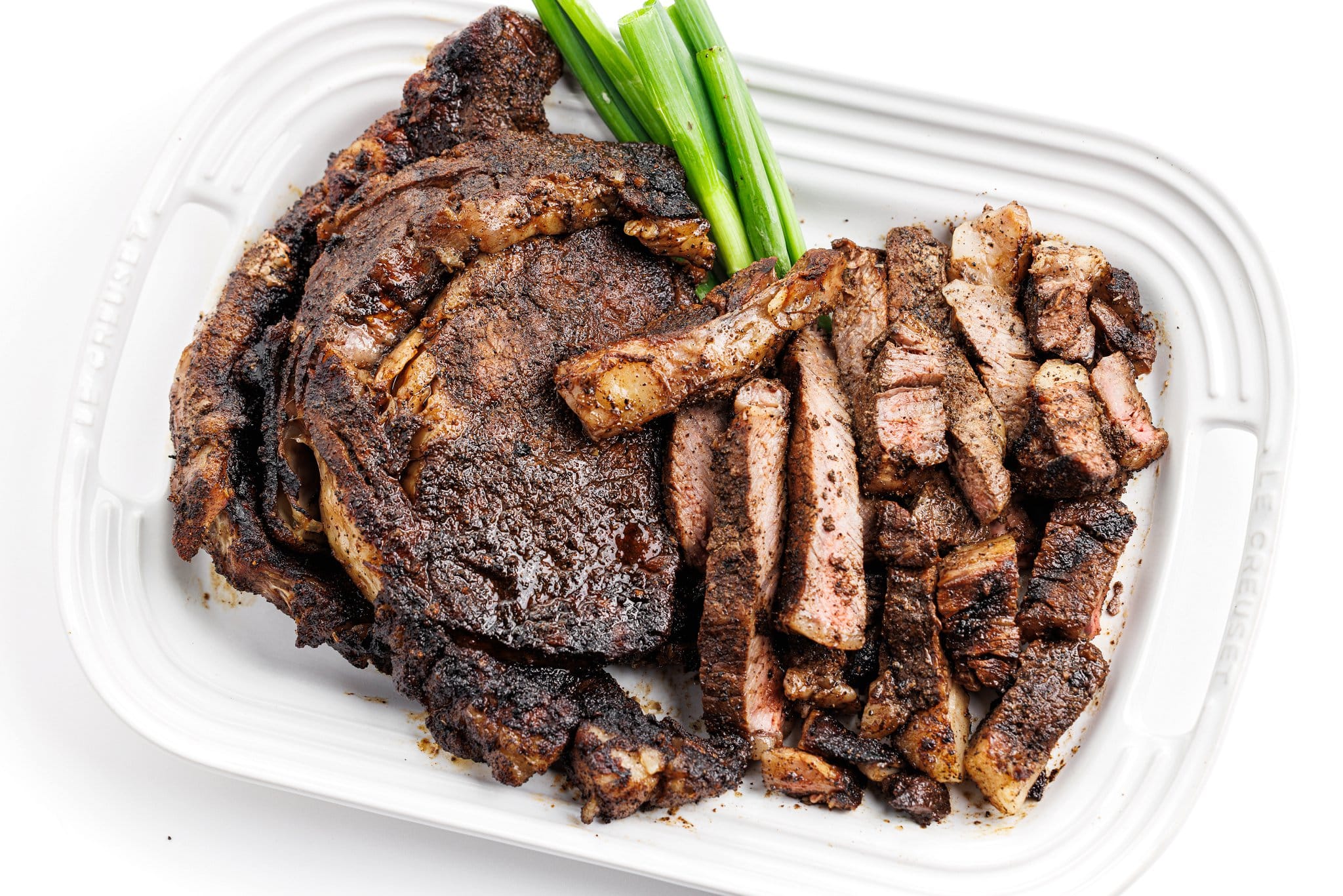 Coffee crusted ribeyes with cut up ribeye on a platter with green onion.