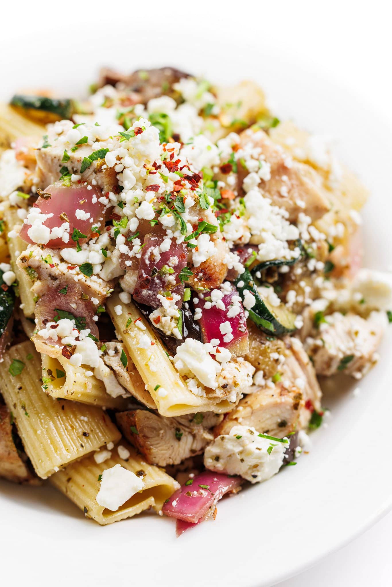 Grilled chicken and vegetable pasta salad topped with chili flakes, parsley, and feta.