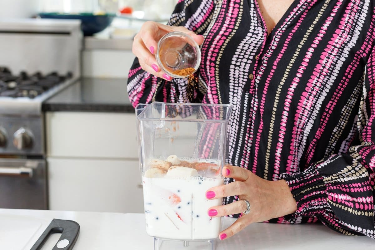 Adding cinnamon to a blender with yogurt and berries.