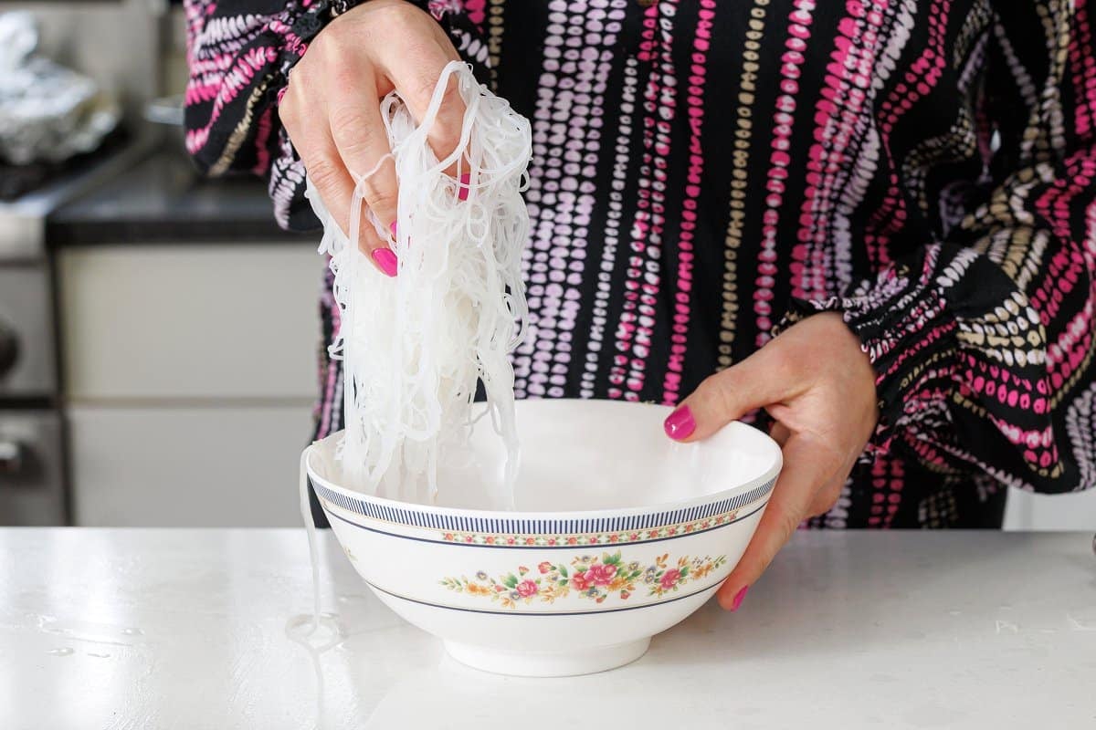 Adding cooked rice noodles to a bowl.