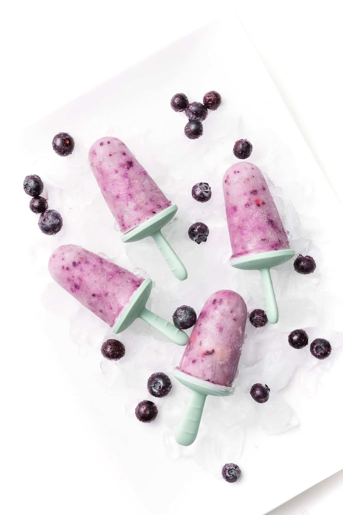 Greek yogurt berry popsicles on a plate with ice and blueberries.