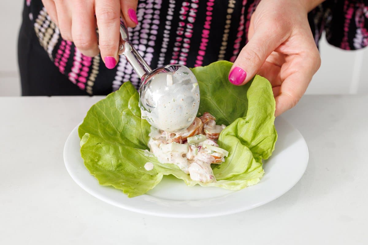 Using an ice cream scoop to scoop shrimp salad onto a leaf of lettuce.