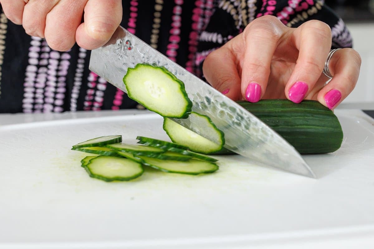 Slicing cucumber into thin slices on a cutting board.