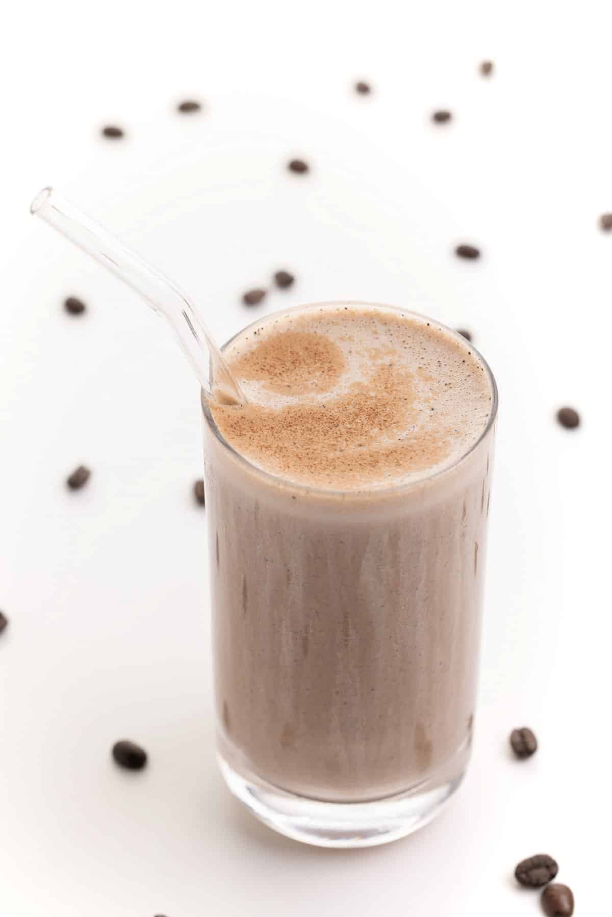 Coffee banana protein smoothie in a glass with a straw.