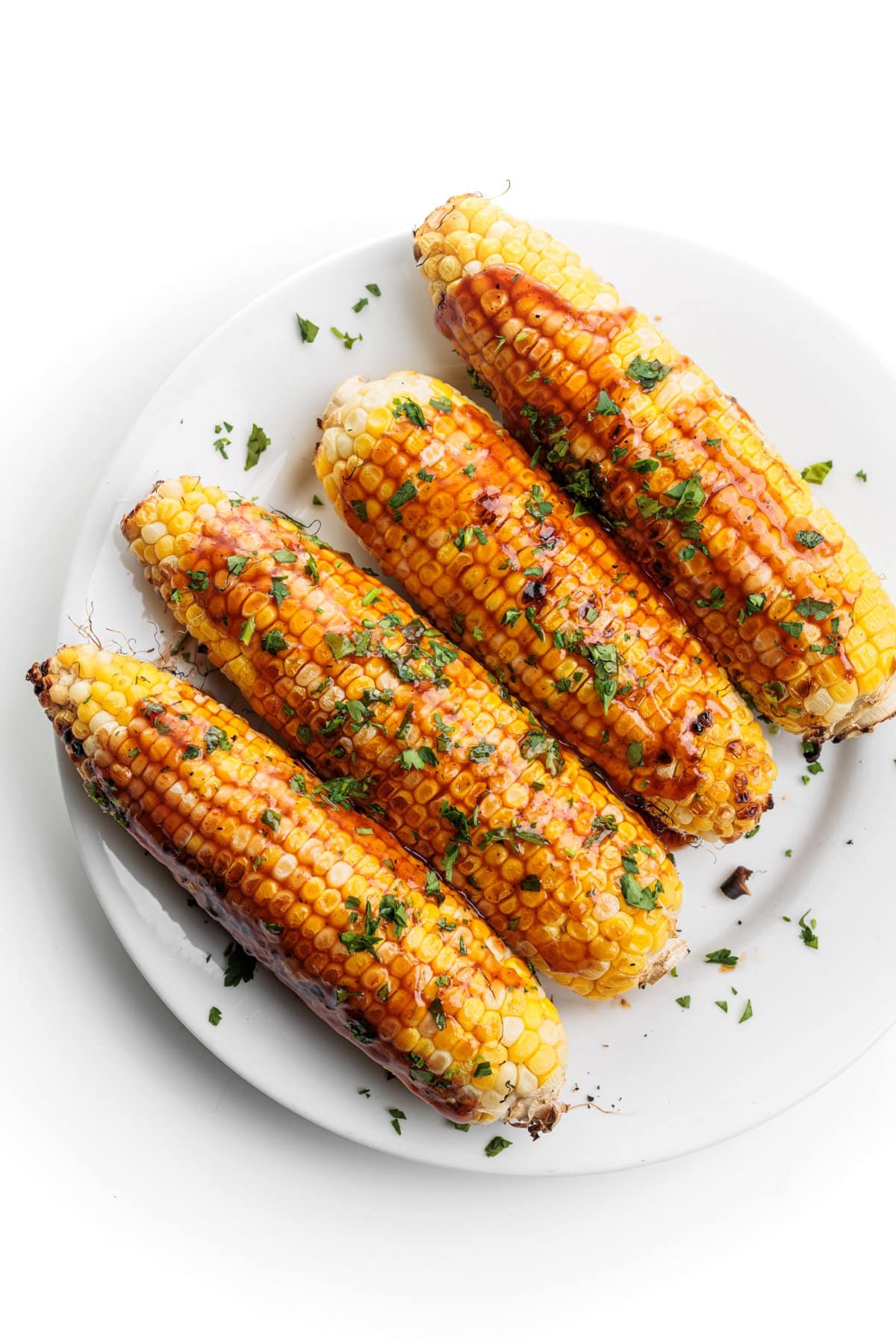 Grilled corn with BBQ sauce on a round white plate.