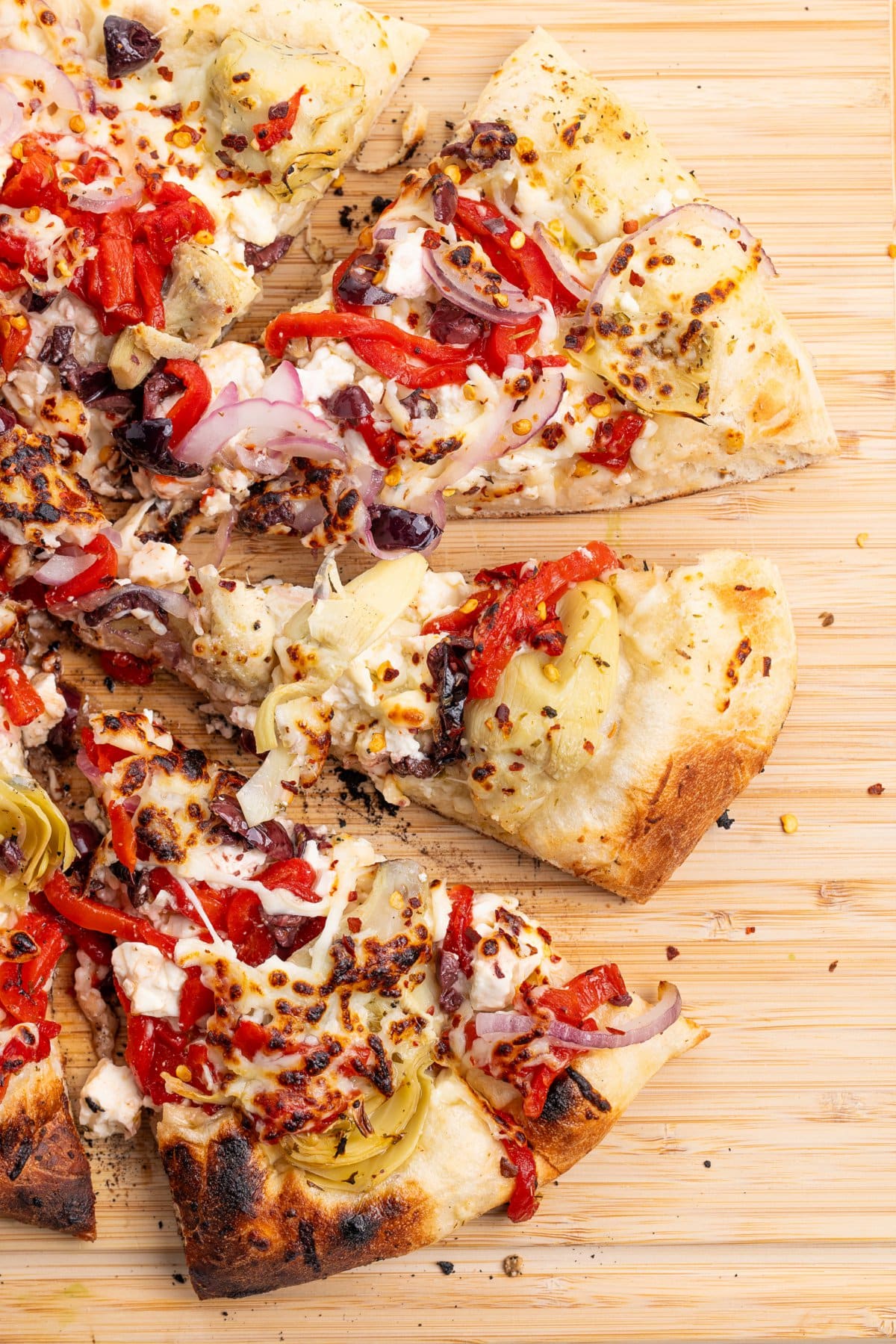 Four slices of Mediterranean veggie pizza on a cutting board.