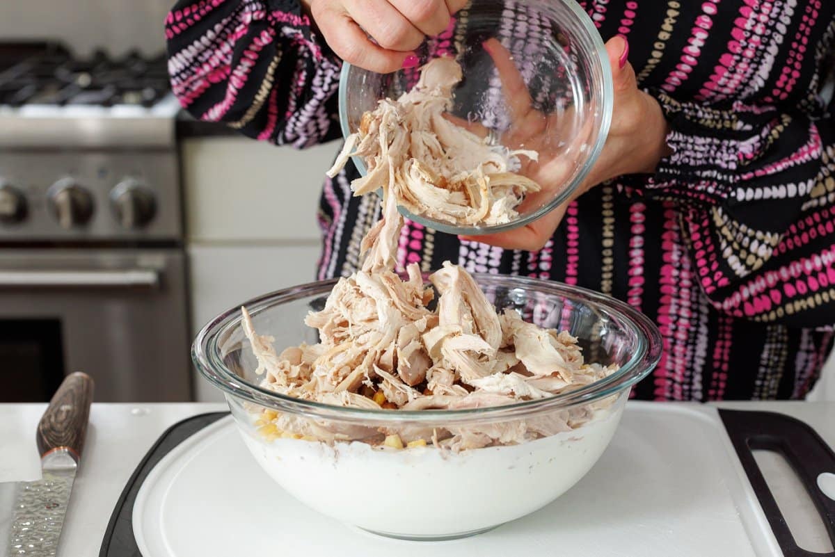 Adding shredded chicken to lasagna filling.