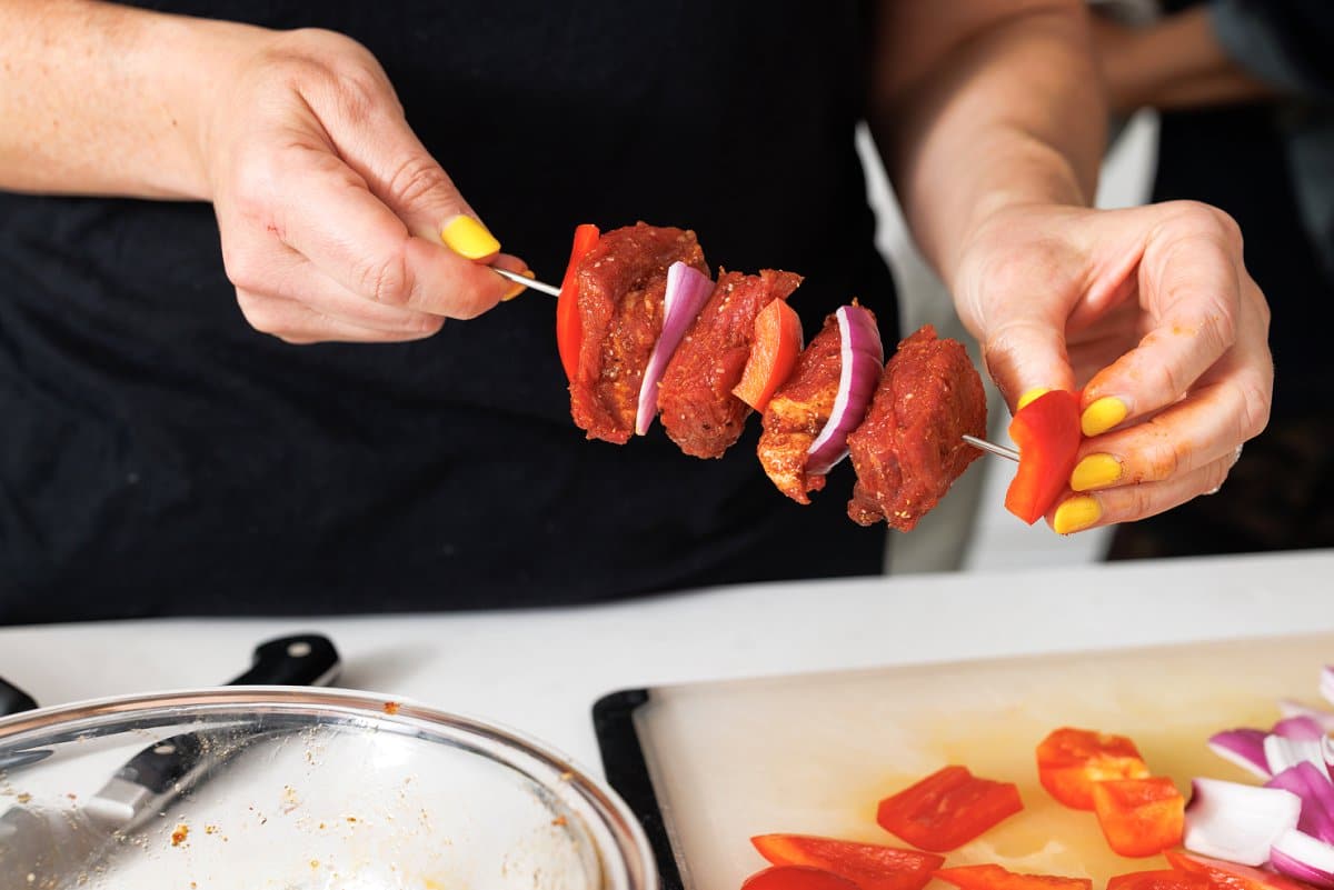 Layering steak, bell pepper, and onion on a skewer.
