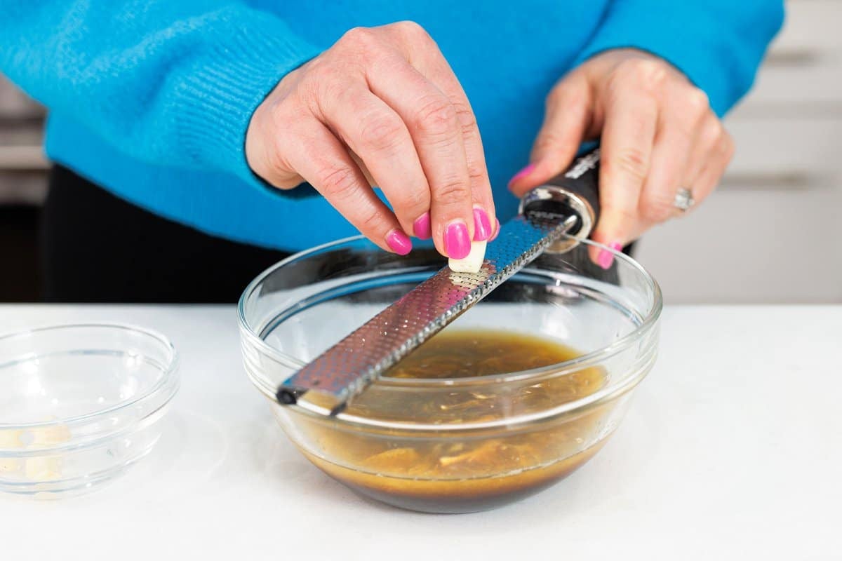 Using a microplane to grate garlic into a bowl.