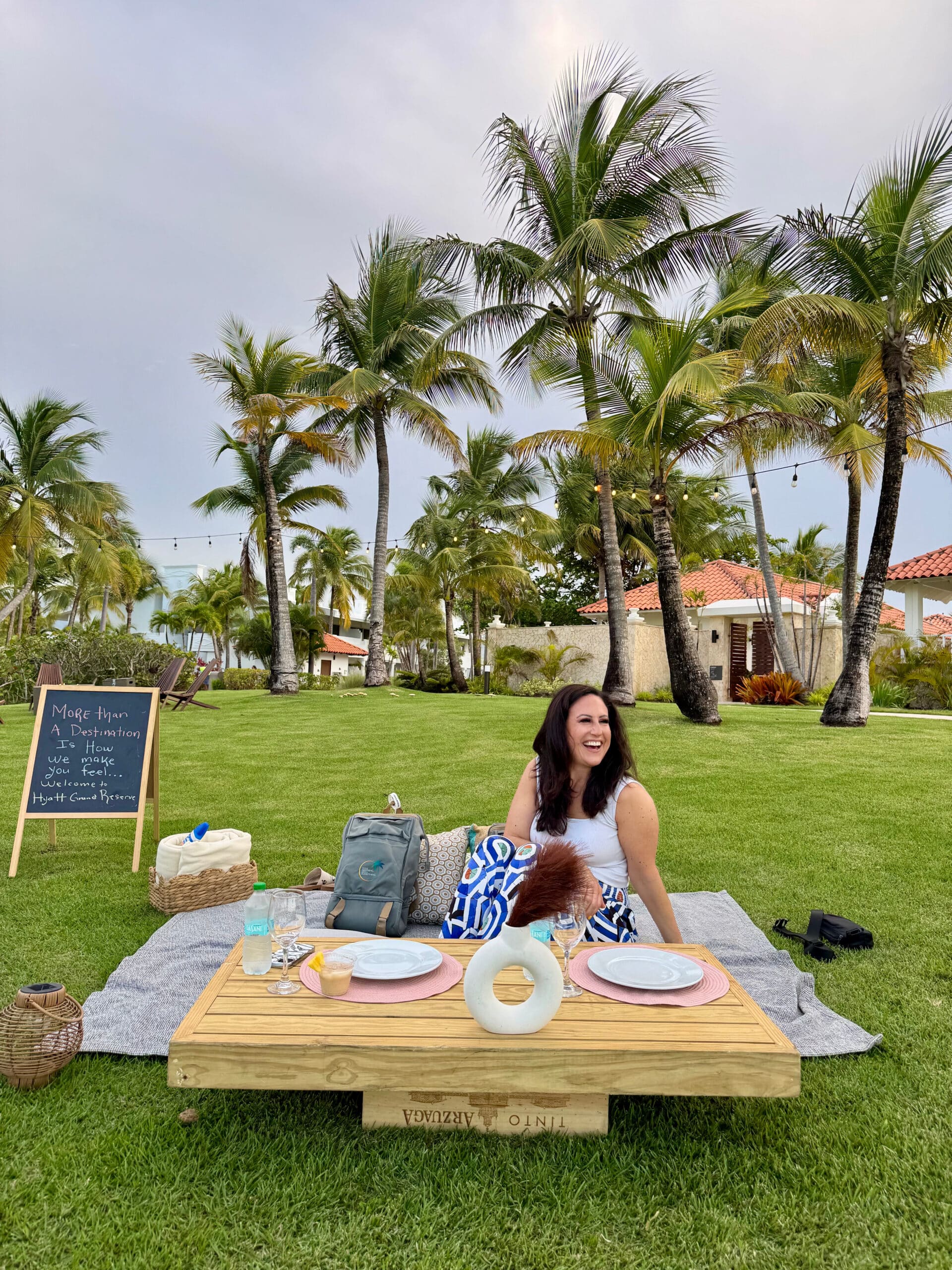 Liz enjoying a picnic dinner on the beach with palm trees and string lights in the background.