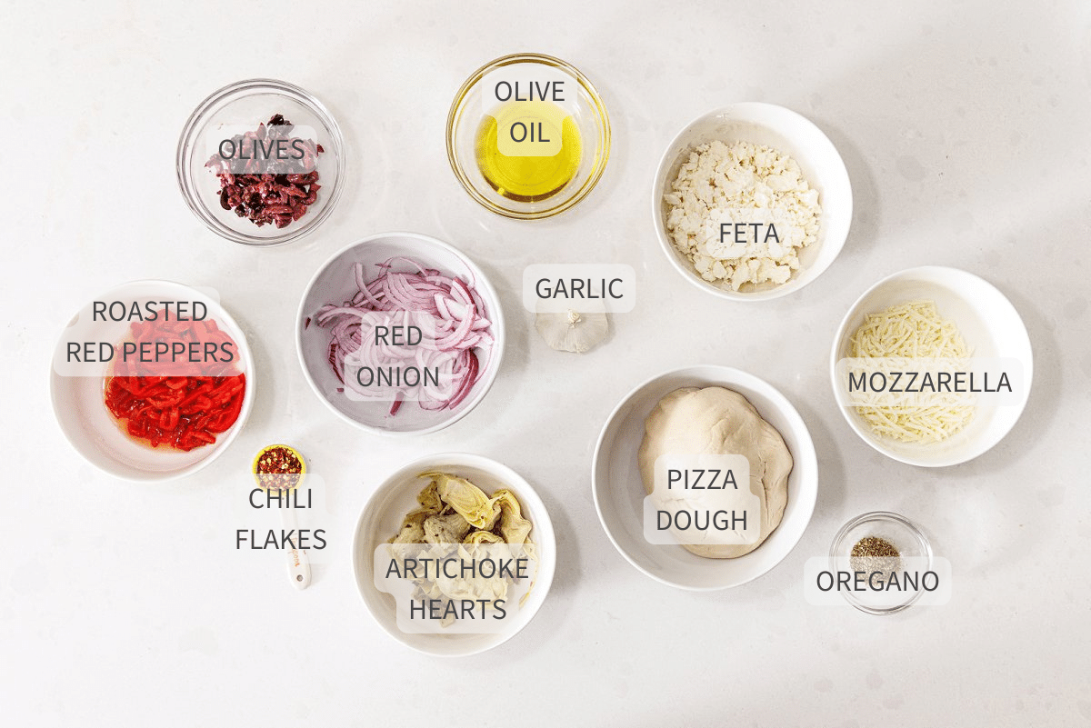Labeled ingredients for Mediterranean veggie pizza on a white counter.