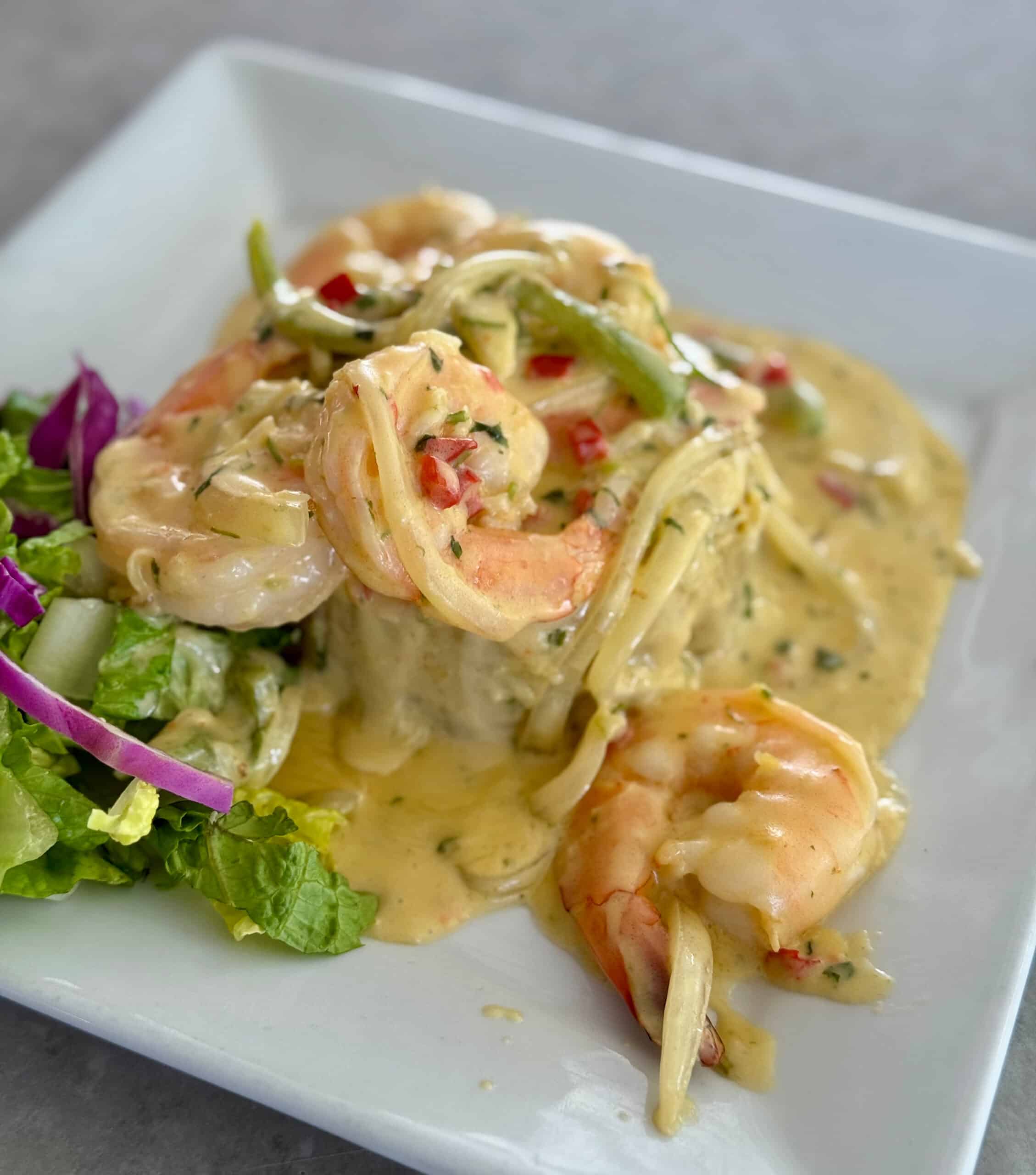 Shrimp pasta on a square plate with fresh veggies.