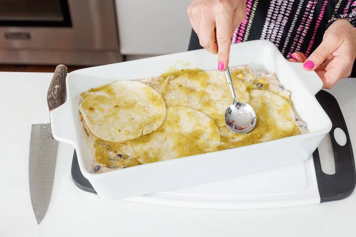 Spreading salsa verde over the top of tortillas with a sppon.