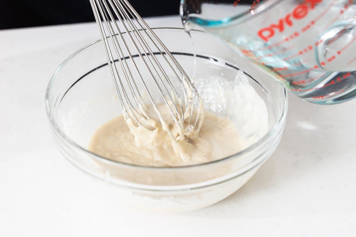 Whisking tahini sauce in a large bowl.