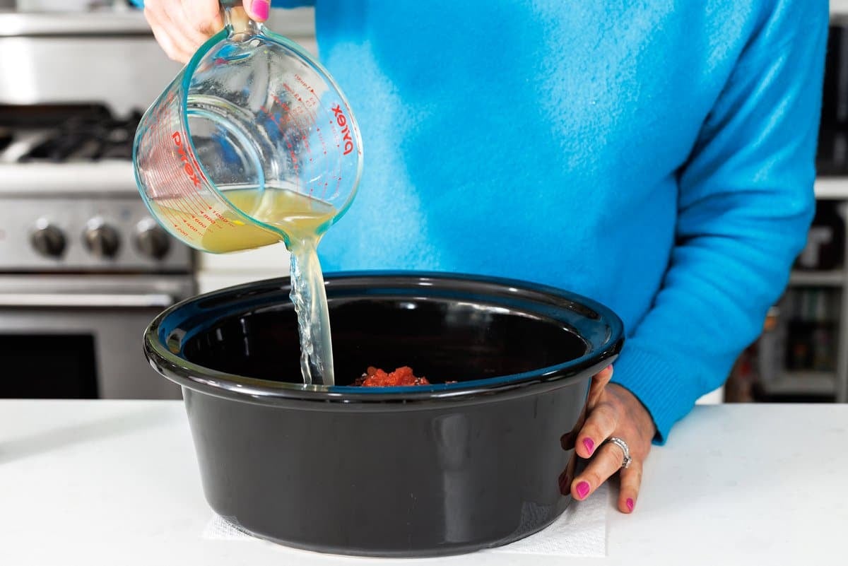 Pouring chicken broth into slow cooker.