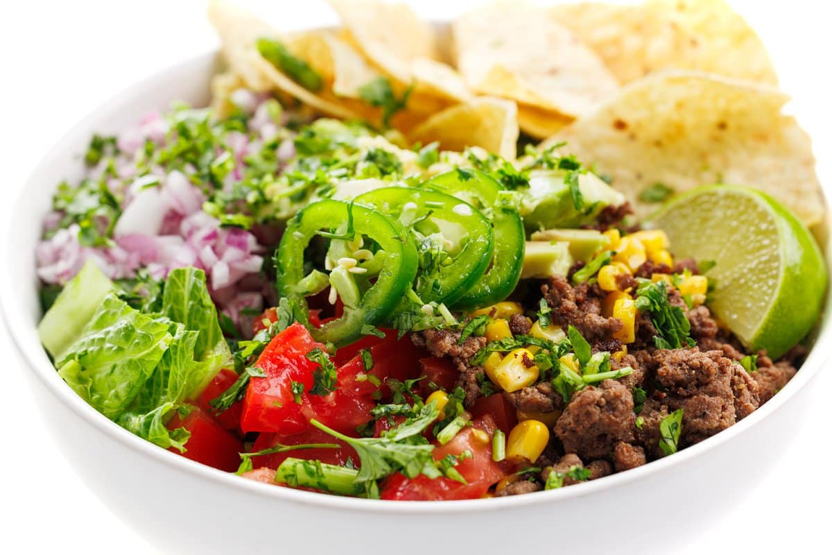 Ground beef taco salad bowl with fresh herbs, a lime slice, and tortilla chips.