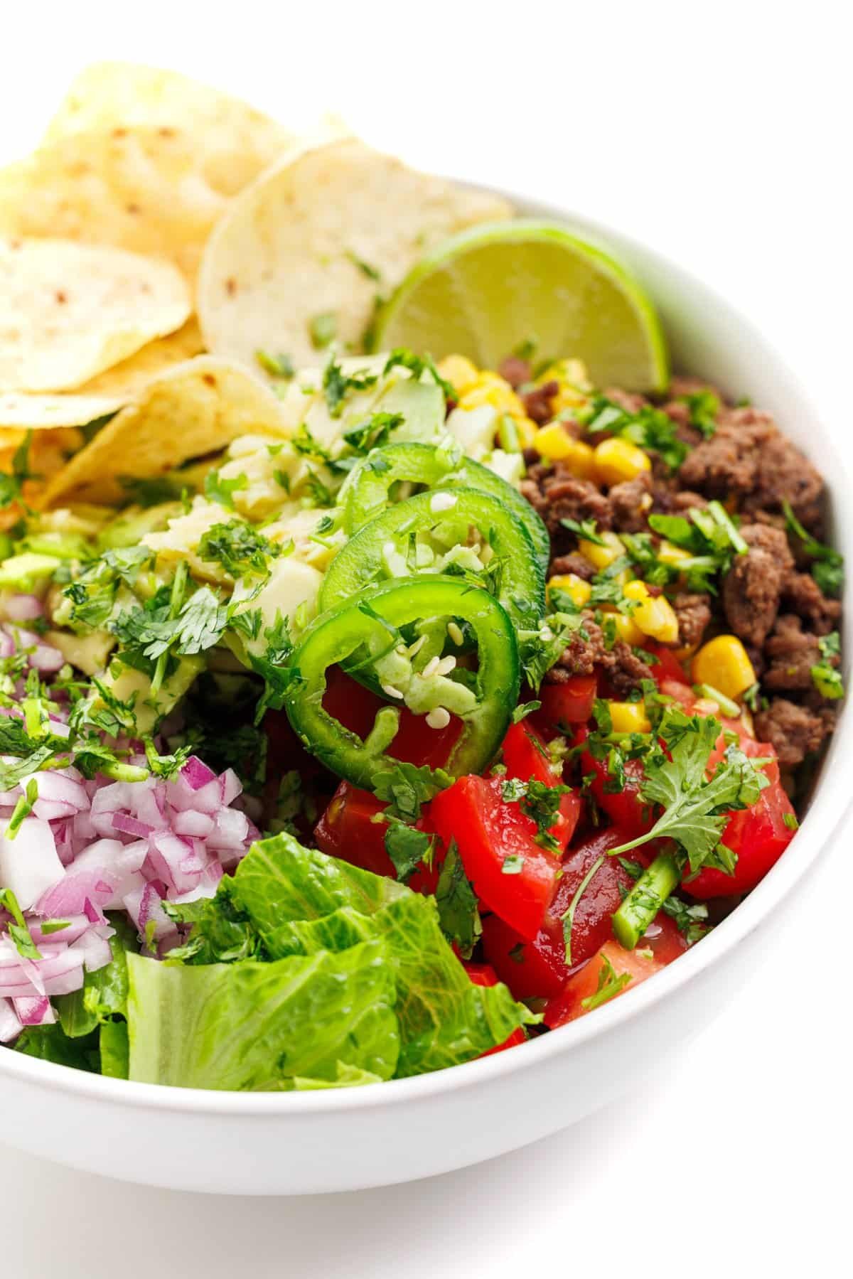 Ground beef taco salad bowl topped with jalapeño slices and fresh herbs.