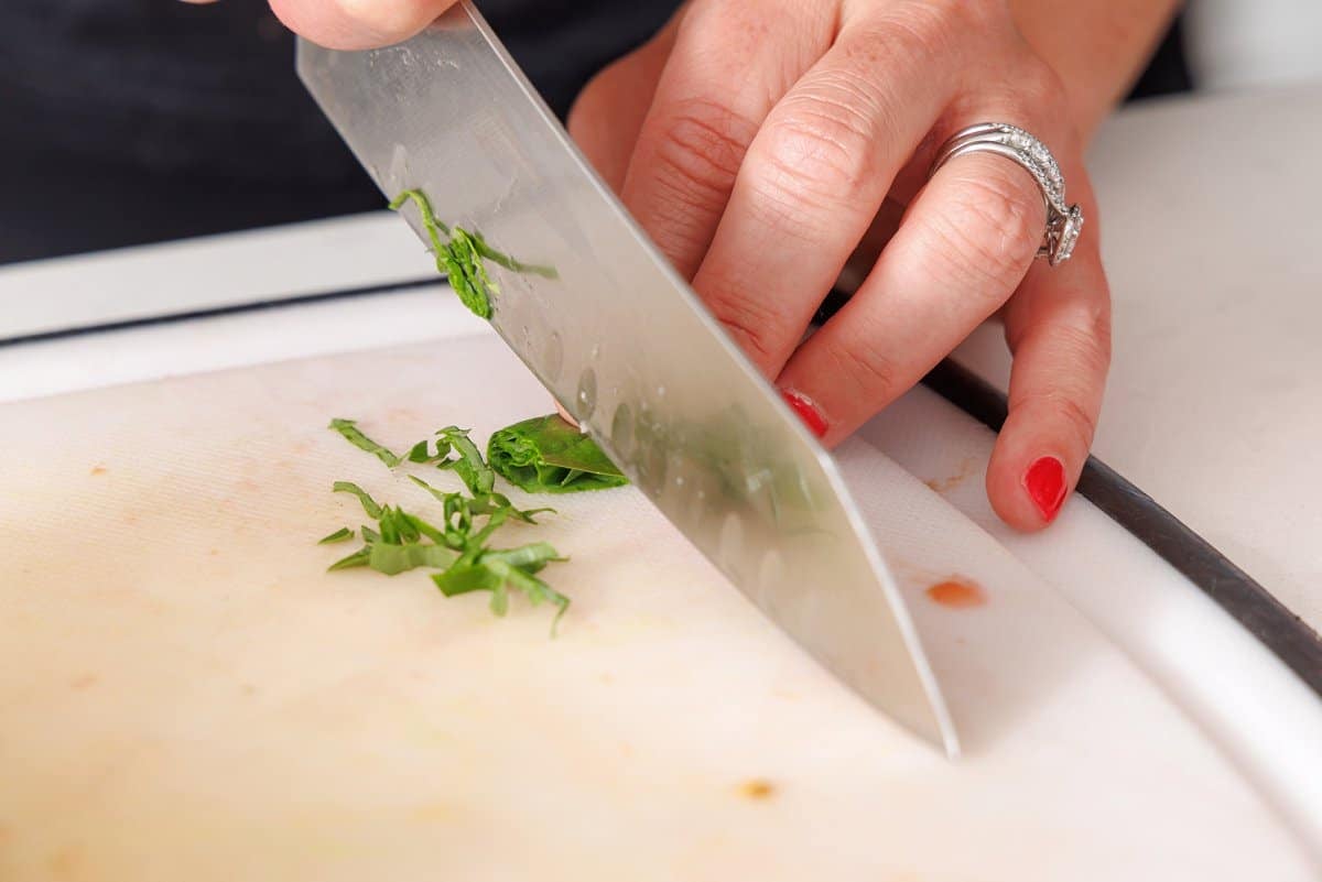 Mincing fresh basil with a sharp knife.