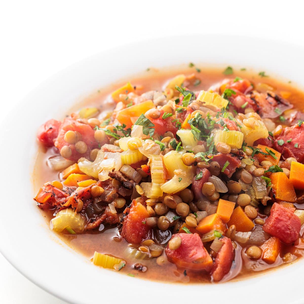 Slow cooker lentil soup with bacon in a white bowl.