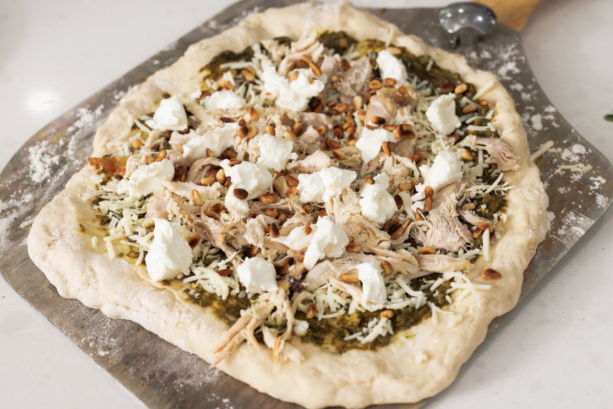 Pesto pizza topped with shredded chicken and goat cheese.
