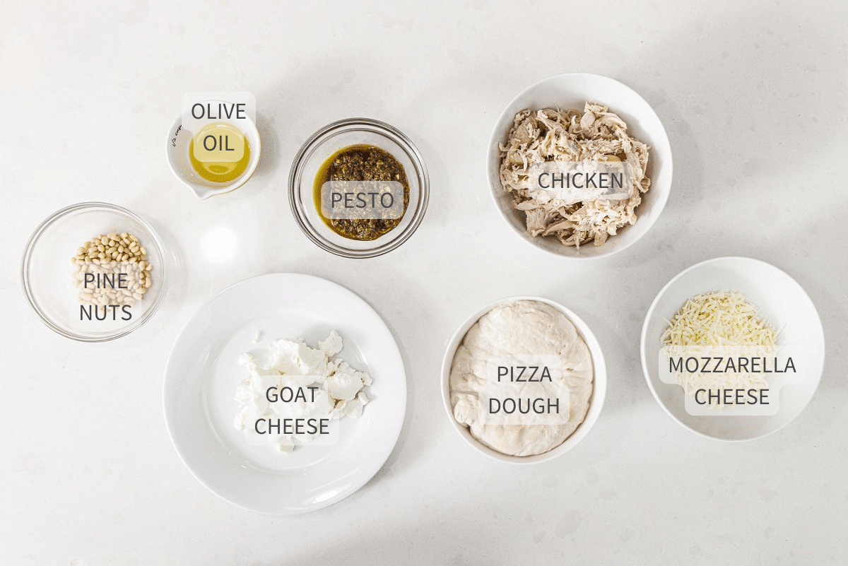 Labeled ingredients for pesto chicken pizza against a white counter top.
