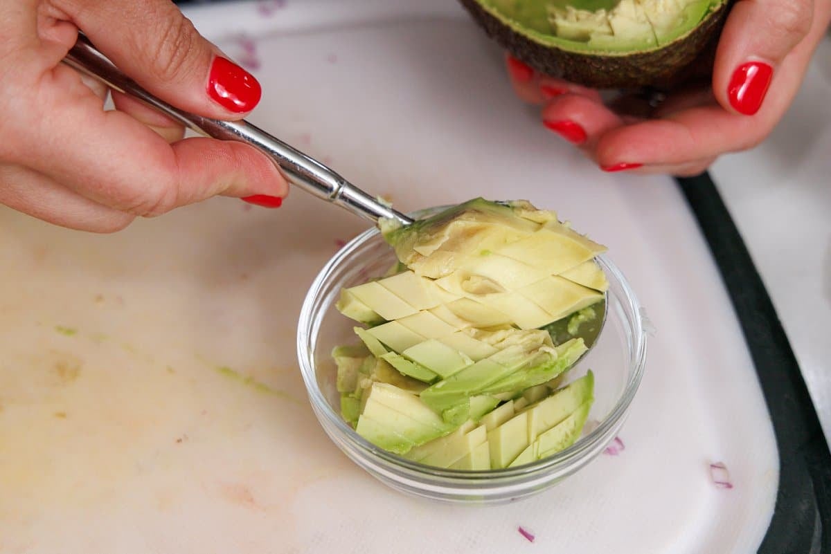 Scooping avocado into a small glass bowl.