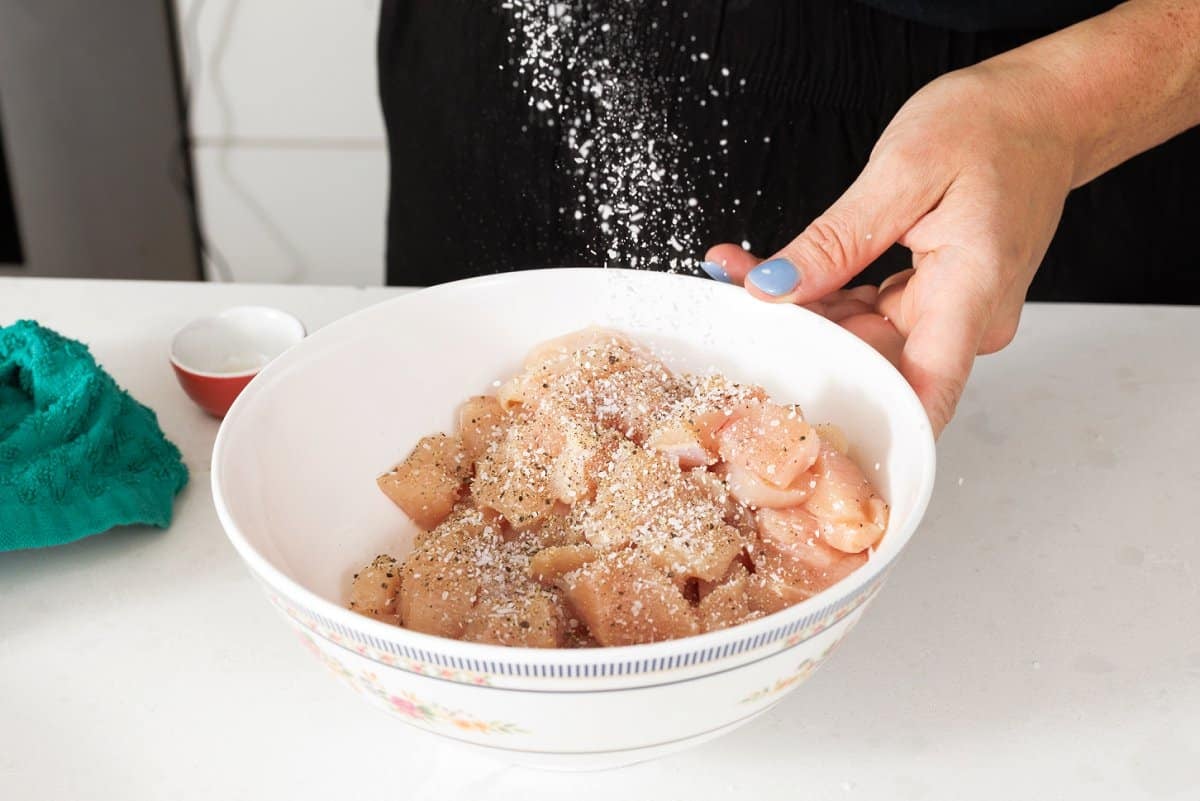 Seasoning raw chicken with salt and pepper.