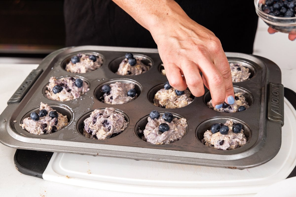 Topping muffin mix in muffin tin with fresh blueberries.