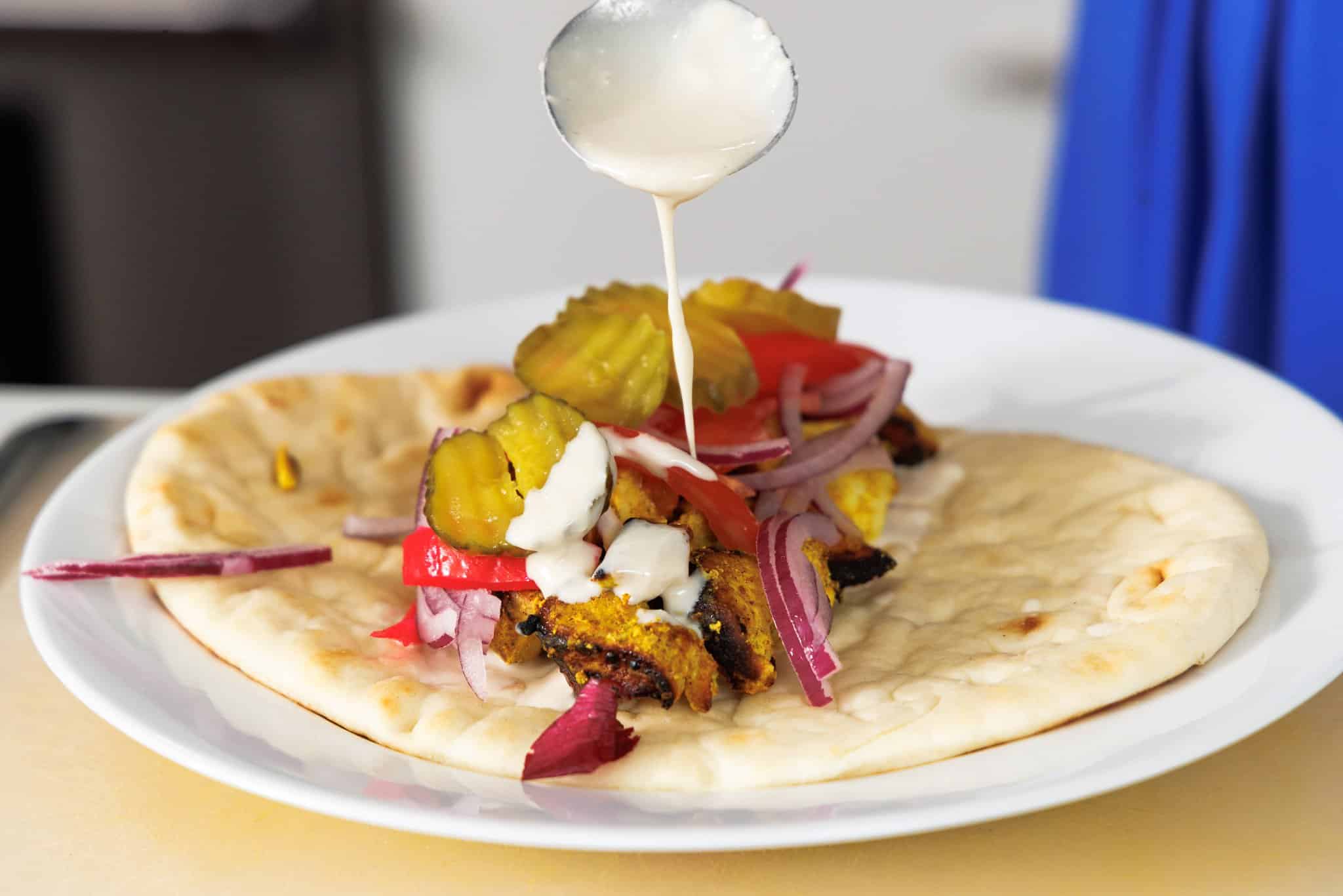 Drizzling tahini sauce over chicken shawarma wrap.