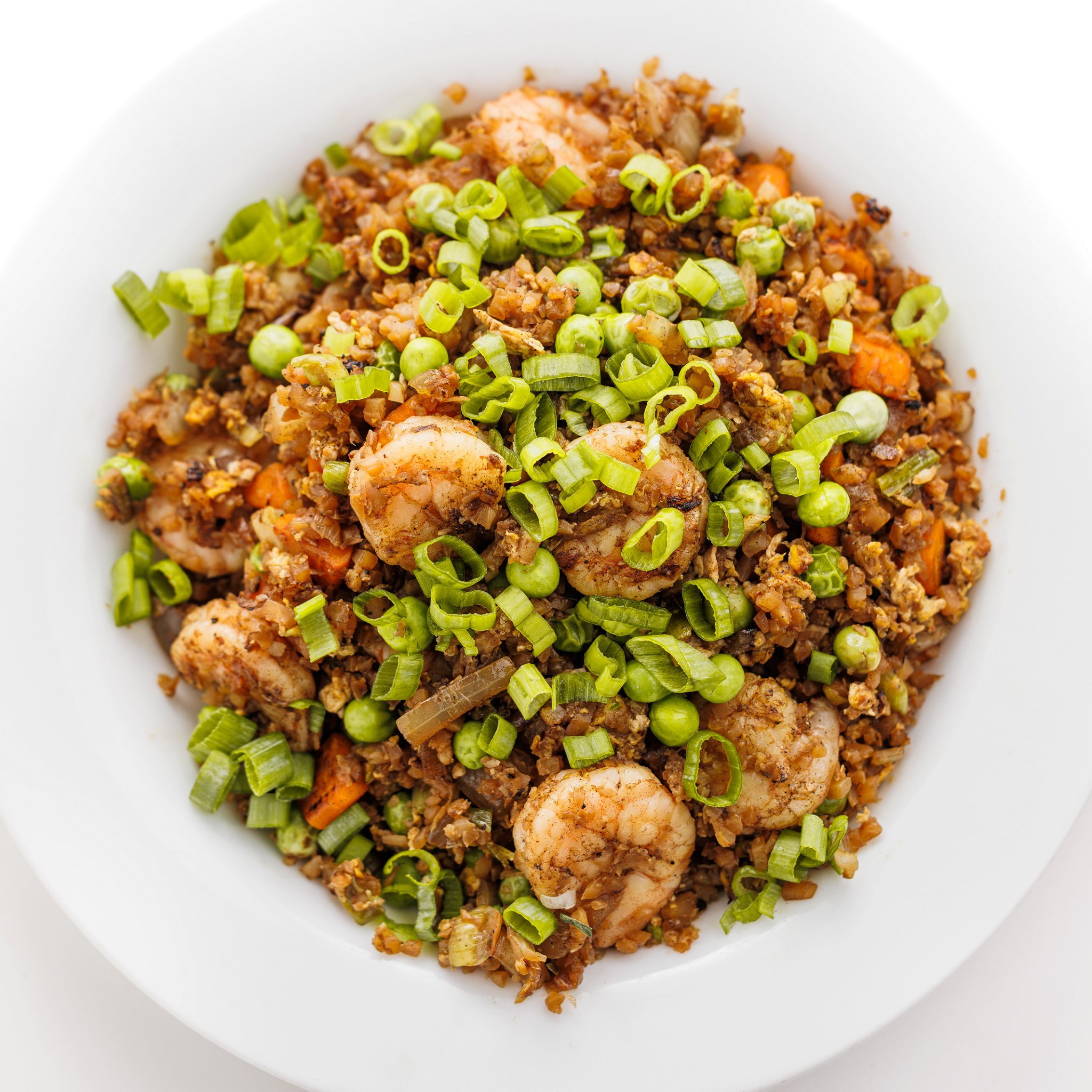 Cauliflower shrimp fried rice garnished with scallions on a plate.